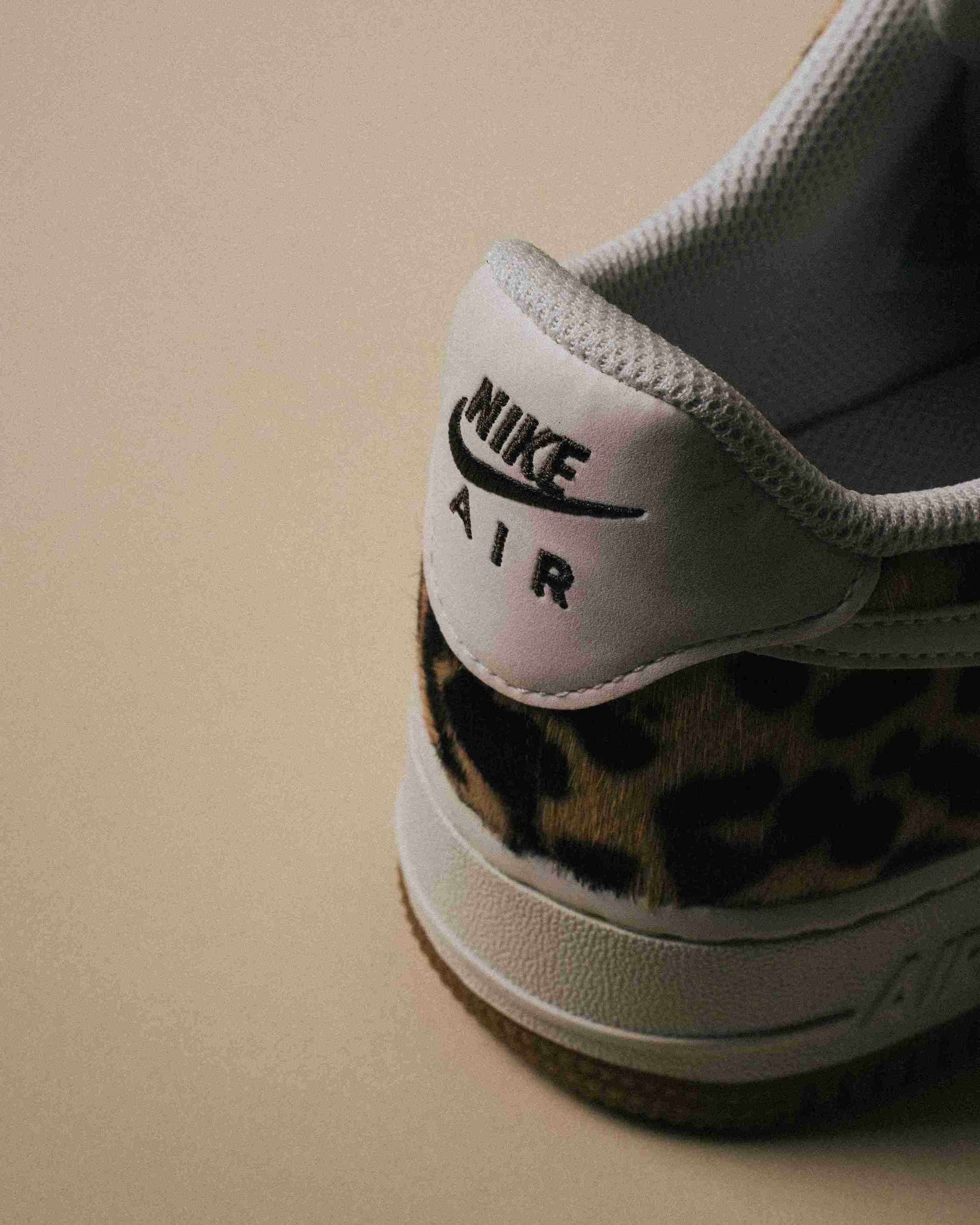 Paire de sneakers Nike Air Force 1 à motif léopard, placée à côté d’une boîte Nike grise sur un fond beige, vue artistique avec lumière douce.